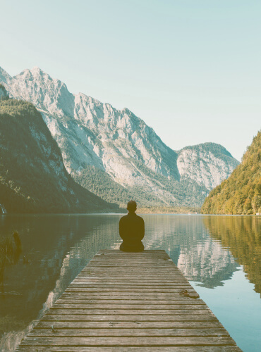 man sitting on the enge of the lake and looking to the mountains